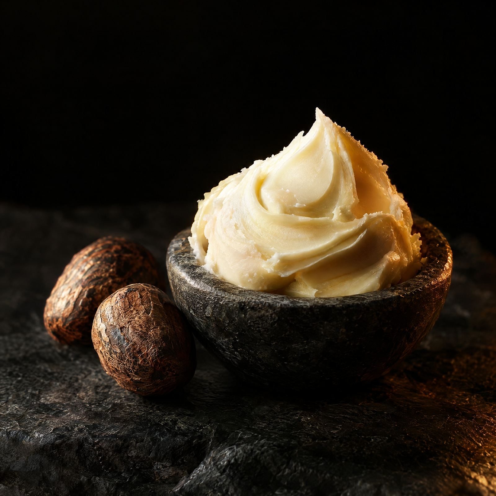 A swirl of shea butter beside raw shea nuts